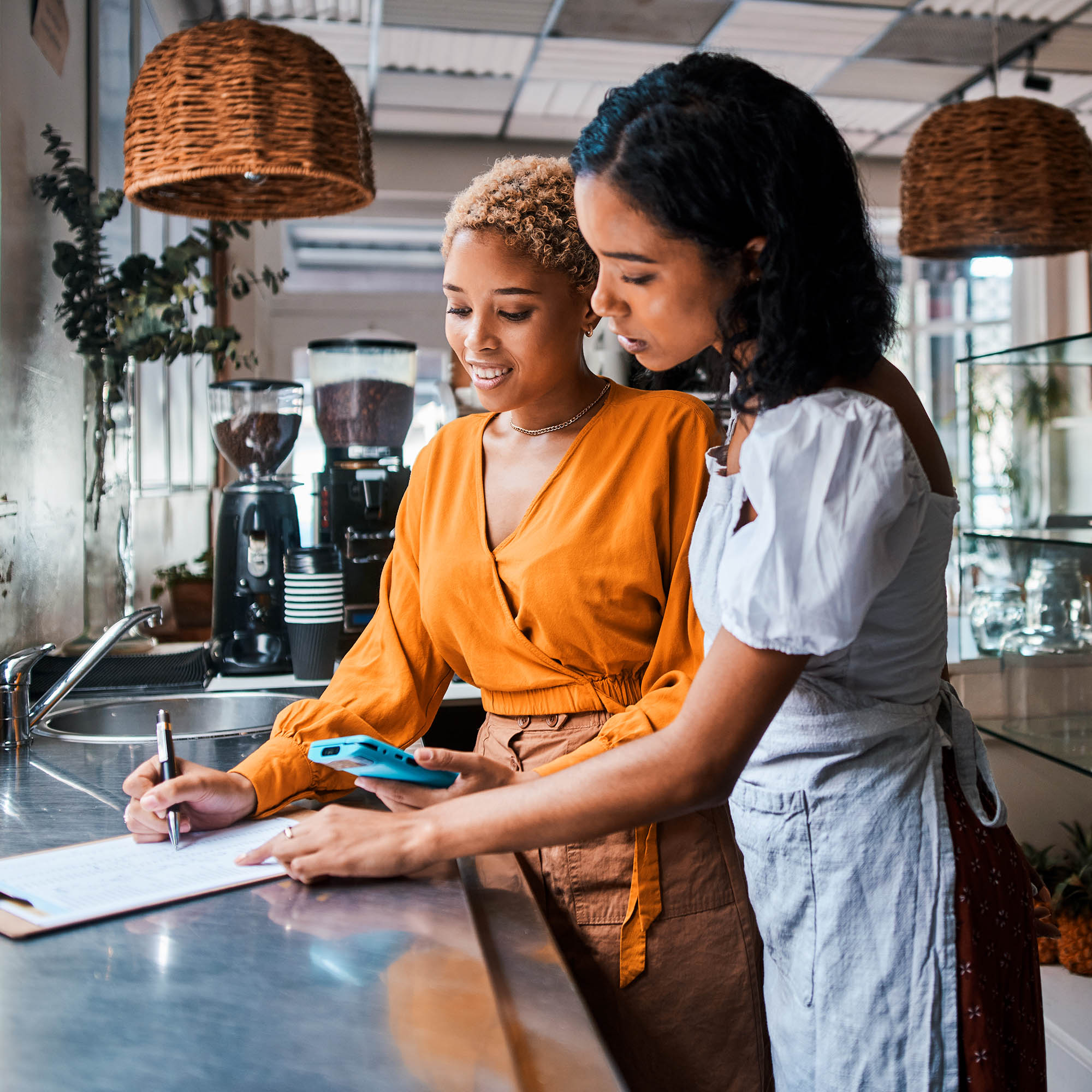 Two women stand at a counter and look at a clipboard.